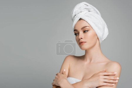 young woman with bare shoulders and towel on head standing with crossed arms isolated on grey 
