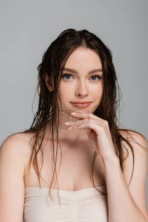 Porträt einer jungen, lächelnden Frau mit nassen Haaren, die isoliert auf grau in die Kamera blickt 