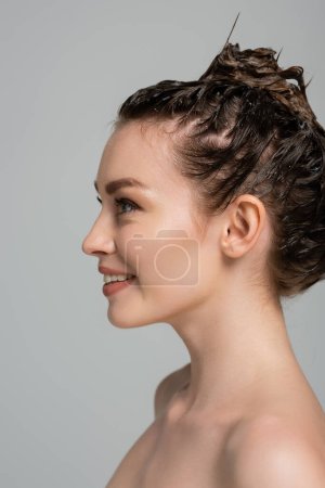 joyeuse jeune femme avec mousse sur la tête regardant loin tout en lavant les cheveux isolés sur gris 