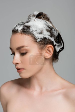 mujer joven con el pelo espumoso y húmedo aislado en gris 