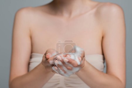Téléchargez les photos : Vue recadrée d'une jeune femme tenant de la mousse blanche dans des mains isolées sur du gris - en image libre de droit