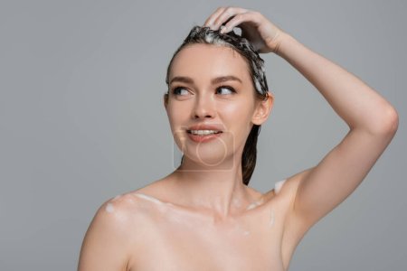 fröhliche junge Frau wäscht schaumiges Haar isoliert auf grau