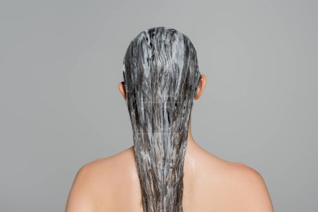 Rückseite der jungen Frau mit nackten Schultern und Maske auf nassem Haar isoliert auf grau 