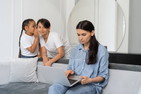 mother using laptop near asian kids talking at home 