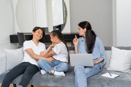 Asian kids having fun while serious mother with laptop pointing with finger at home 