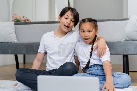 Shocked asian children watching movie on blurred laptop at home 