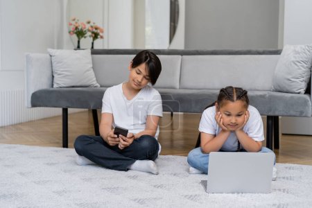 Asiática chica viendo película en el ordenador portátil mientras hermano usando smartphone en casa 