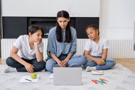 Téléchargez les photos : Asiatiques enfants avec des pommes regardant ordinateur portable près de maman et crayons de couleur à la maison - en image libre de droit