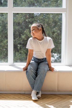 Positive asian girl sitting on windowsill at home 