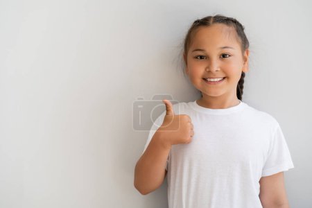 Sonriendo chica asiática mostrando como gesto y mirando a la cámara en casa 