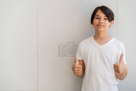preadolescente asiático chico mostrando como gesto cerca de pared en casa 