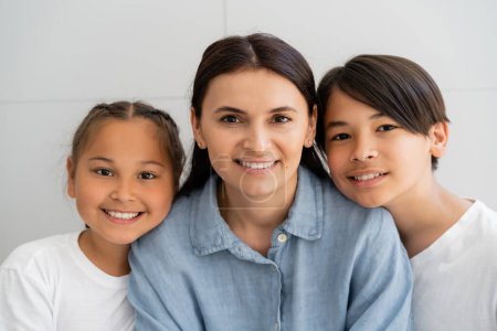 Photo for Positive woman and asian children looking at camera near wall at home - Royalty Free Image