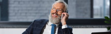 Hombre de negocios sonriente en ropa formal hablando en el teléfono inteligente en la oficina, pancarta 