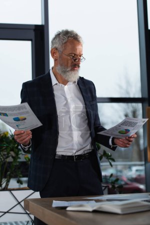 Photo for Focused businessman in suit looking at charts in office in evening - Royalty Free Image