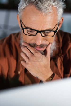 Photo for Mature businessman in eyeglasses looking at blurred computer monitor in office - Royalty Free Image