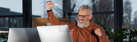 Téléchargez les photos : Homme d'affaires d'âge moyen montrant un geste oui près de l'écran d'ordinateur dans le bureau en soirée, bannière - en image libre de droit