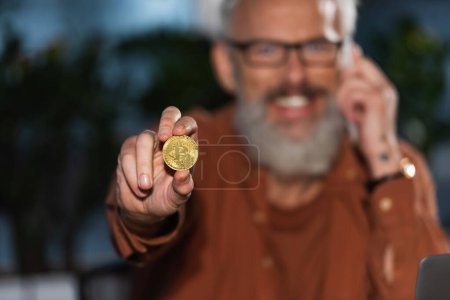 Foto de KYIV, UCRANIA - 17 de noviembre de 2022: enfoque selectivo de bitcoin de oro en la mano del empresario de mediana edad feliz - Imagen libre de derechos
