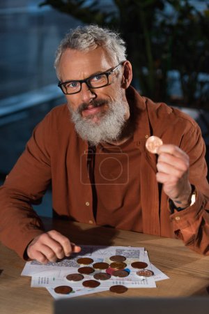 Photo for KYIV, UKRAINE - NOVEMBER 17, 2022: businessman in eyeglasses holding bitcoin and looking at camera - Royalty Free Image
