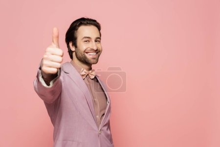 Cheerful host of event looking at camera and showing like gesture isolated on pink 