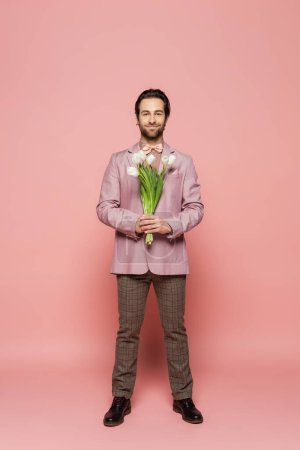 Volle Länge der stilvollen Gastgeber der Veranstaltung hält Strauß von Tulpen auf rosa Hintergrund 