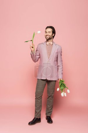 Téléchargez les photos : Élégant hôte de l'événement tenant bouquet de tulipes blanches sur fond rose - en image libre de droit