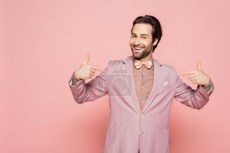 Positive host of event in jacket pointing with fingers on pink background 