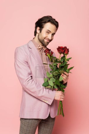 Photo for Positive host of event in jacket and bow tie holding roses on pink background - Royalty Free Image