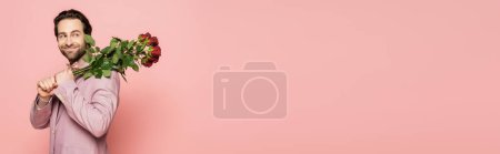 Photo for Smiling brunette host of event holding roses and looking away isolated on pink, banner - Royalty Free Image