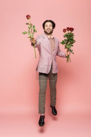 Excited host of event holding roses while jumping on pink background 