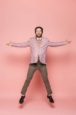 Photo for Positive and stylish host of event looking at camera while jumping on pink background - Royalty Free Image
