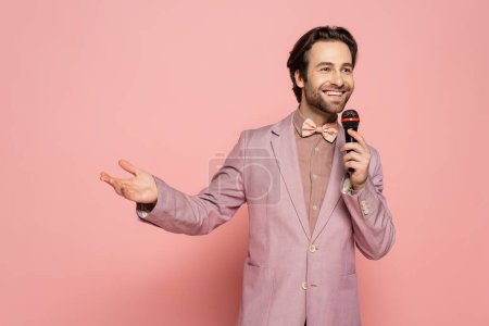 Photo for Positive host of event talking and holding microphone on pink background - Royalty Free Image