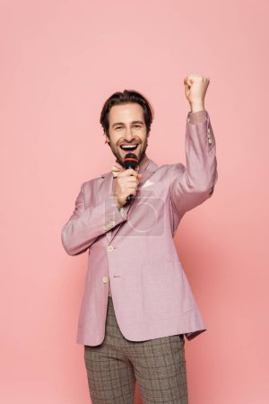 Excited host of event showing yes gesture and talking at microphone on pink background 