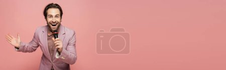 Photo for Stylish host of event holding microphone and waving hand at camera isolated on pink, banner - Royalty Free Image