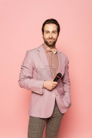 Portrait de l'hôte de l'événement en n?ud papillon et veste tenant microphone isolé sur rose 