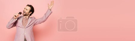 Photo for Stylish host of event singing at microphone on pink background, banner - Royalty Free Image
