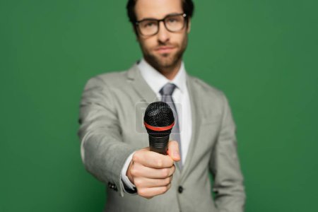 Photo for Blurred newscaster in suit holding microphone isolated on green - Royalty Free Image