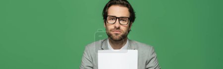 young broadcaster in eyeglasses and suit holding blank paper isolated on green, banner 