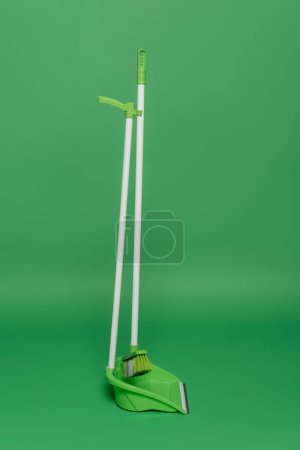broom and plastic scoop on green background, housekeeping concept 