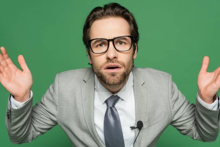 Emotionaler Nachrichtensprecher in Brille und Anzug gestikuliert isoliert auf Grün 