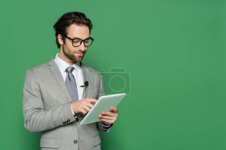 periodista en gafas y traje usando tableta digital aislada en verde 