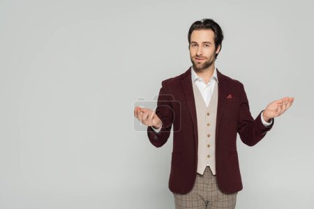 Photo for Young showman in elegant attire looking at camera while gesturing isolated on grey - Royalty Free Image