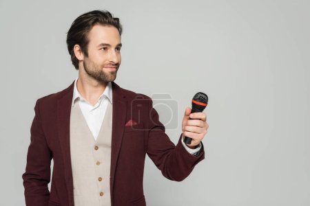 host of event in red blazer holding microphone isolated on grey
