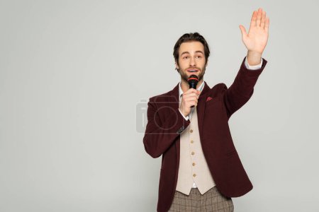 Showman in offizieller Kleidung spricht in Mikrofon und zeigt Stop-Geste isoliert auf grau 