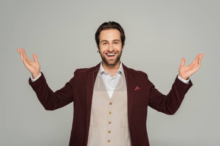 Photo for Amazed showman in red blazer gesturing while looking at camera isolated on grey - Royalty Free Image