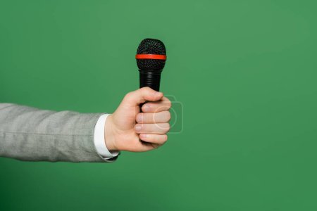 cropped view of journalist holding microphone in hand isolated on green 