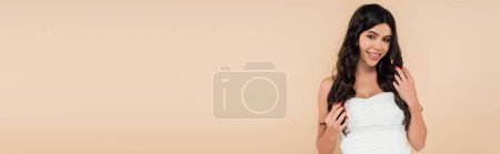 Happy woman in white top touching healthy hair isolated on beige, banner 
