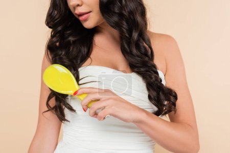 Foto de Cropped view of woman in top combing wavy hair isolated on beige - Imagen libre de derechos