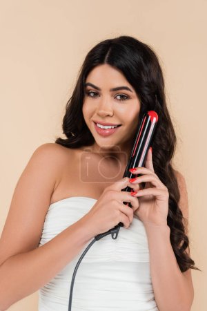 Photo for Smiling woman using curling iron and looking at camera isolated on beige - Royalty Free Image