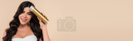 Photo for Smiling brunette woman holding hairspray isolated on beige with copy space, banner - Royalty Free Image