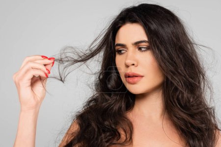 sad woman looking at long and damaged hair isolated on grey
